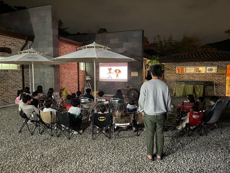밤, 야외 스크린 앞에 앉은 아이들과 어른(뒷모습)